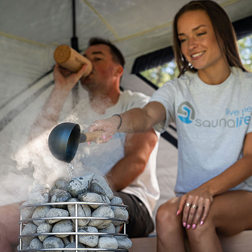 Water being ladled onto the stones of a SaunaLife Titan SL1 inside a SaunaTrekker sauna tent