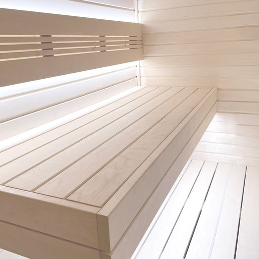Sauna interior with light slatted wall paneling, a backrest, and a wide bench with a lower step, softly lit
