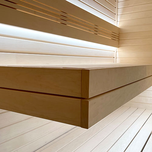 Sauna interior with stacked bench tiers, slatted wall paneling and soft backlit lighting along the walls