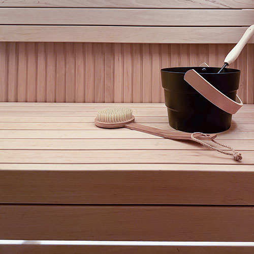Sauna interior with tiered benches, wall paneling, a black bucket with ladle, and a bristle back brush