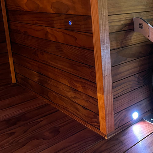 Sauna corner with horizontal wall paneling, a vertical trim board, and small round recessed lights above the floor