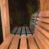 SaunaLife E8 barrel sauna bench beside window at night overlooking lit garden