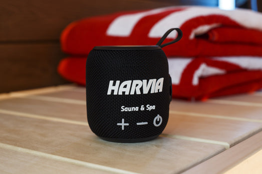 Black Harvia speaker on a sauna bench in front of folded towels