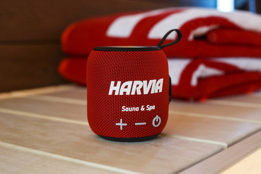 Red Harvia speaker on a sauna bench in front of folded towels