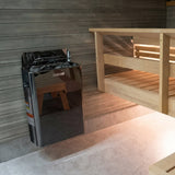 Black Harvia The Wall heater mounted on a gray sauna wall beside wooden benches
