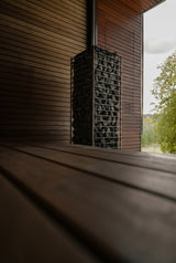 HUUM CLIFF 10.5kW dark-stone heater in a sauna beside a garden-view window