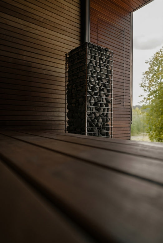 HUUM CLIFF 10.5kW dark-stone heater in a sauna beside a garden-view window