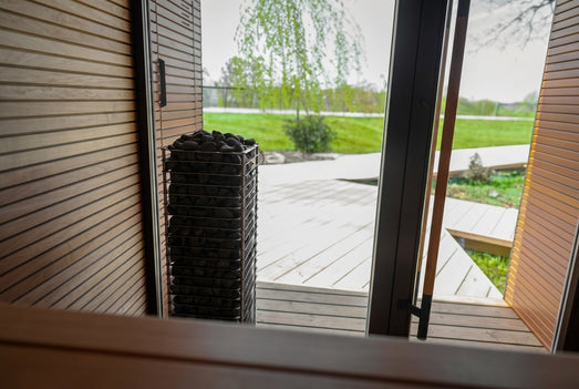 HUUM CLIFF 10.5kW heater in sauna doorway overlooking a green lawn outside