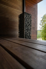 HUUM CLIFF 9kW heater beside a sauna window overlooking green trees