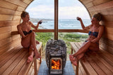Two people relaxing in a barrel sauna with a HUUM wood stove and ocean view
