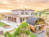 Outdoor barrel sauna with HUUM chimney beside a modern beach house