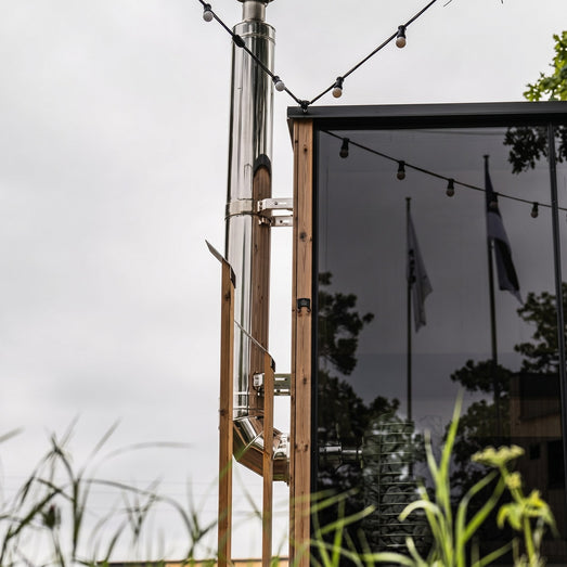 HUUM backside connection chimney running up the side of a glass-front outdoor sauna