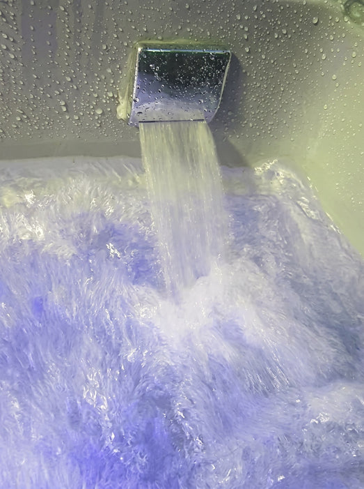 Chrome waterfall faucet pouring into the Mesa WS-501 tub with blue accent lighting
