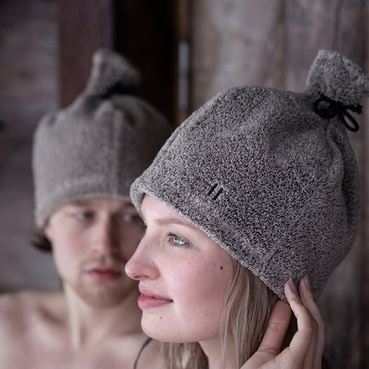 Woman and man wearing Rento linen terry sauna hats in a wooden sauna