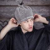 Man in a robe putting on a grey Rento linen terry sauna hat