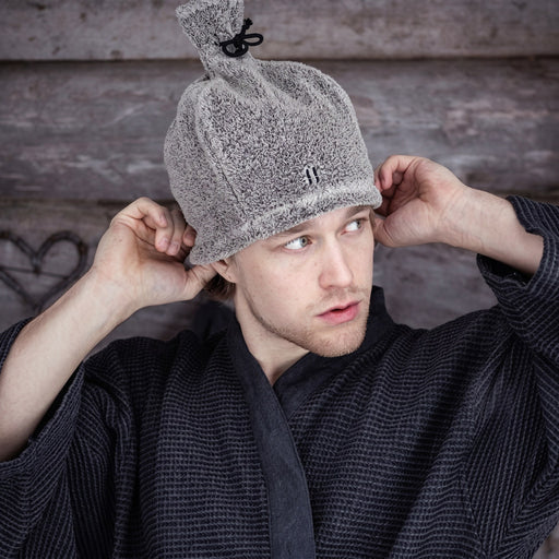 Man in a robe putting on a grey Rento linen terry sauna hat
