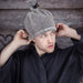 Man in a robe putting on a grey Rento linen terry sauna hat