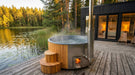 SaunaLife S4 hot tub with lit wood fire on a deck beside a lake and modern cabin