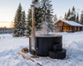 SaunaLife S4 black hot tub steaming in snow at dusk beside a log cabin