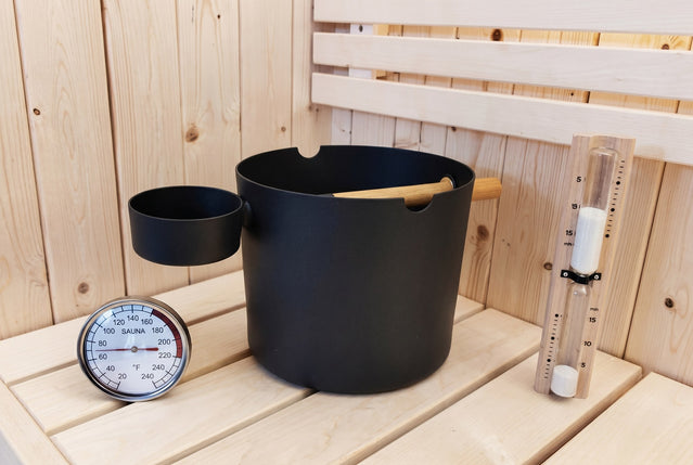 SaunaLife black bucket, ladle, thermometer and sand timer accessory set on a bench