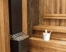 Saunum Air 5 heater in a sauna corner with stone-tiled wall and white pail on bench