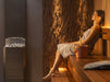 Woman relaxing on a sauna bench beside the Saunum Air 5 heater in ambient light
