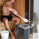 Man ladling water over the Saunum Air 7 heater stones to create steam