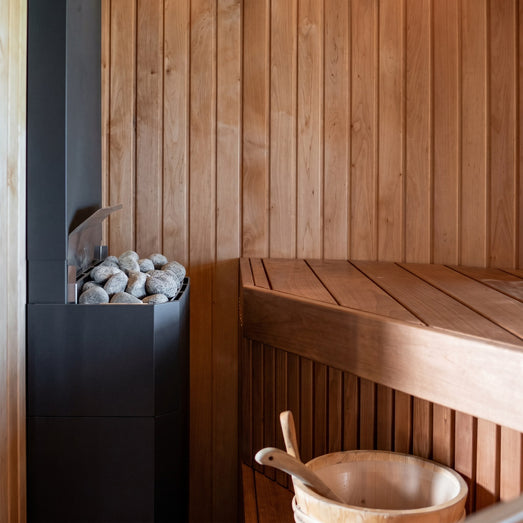 Slim black Saunum Air heater in a cedar sauna corner with a wooden bucket below