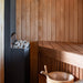 Slim black Saunum Air heater in a cedar sauna corner with a wooden bucket below