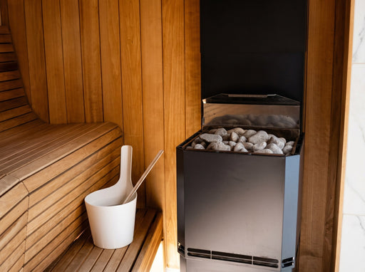 Saunum Air L 10 heater filled with stones beside a white bucket in a cedar sauna