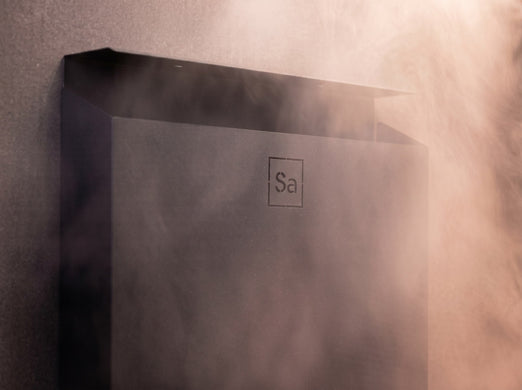 Top corner detail of the black Saunum Air L 10 heater with steam rising in soft light
