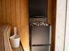 Saunum Air L 13 heater installed in a cedar sauna corner next to a bucket and ladle