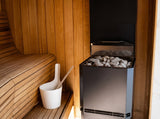 Saunum Air L 13 heater with sauna stones installed beside cedar benches and a water bucket
