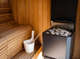 Saunum Air L 15 heater with stones beside cedar benches and a white sauna pail