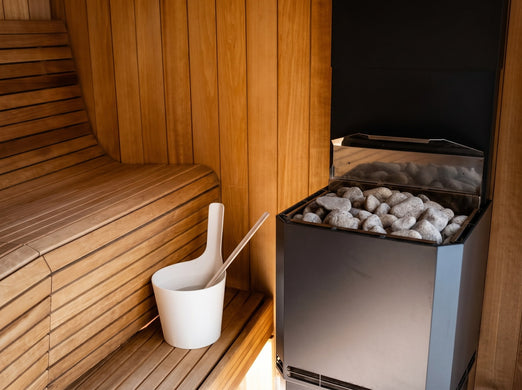 Saunum Air L 15 heater with stones beside cedar benches and a white sauna pail