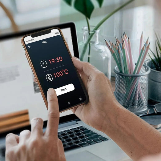 Hand using the Saunum mobile app showing timer and 100C temperature with start button