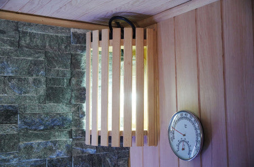 Slatted wall lamp and round thermometer-hygrometer beside the slate-colored stone wall in the SunRay Rockledge sauna