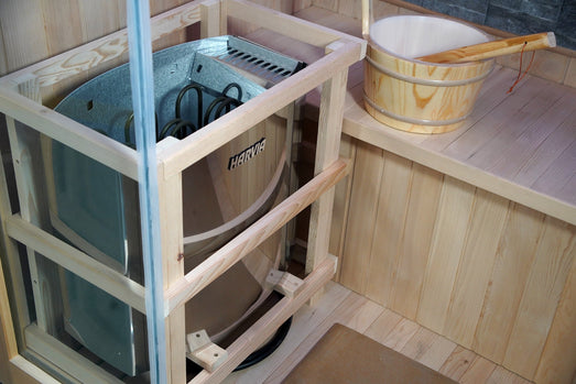 Harvia heater in its wooden guard next to a wooden bucket in the SunRay Westlake sauna